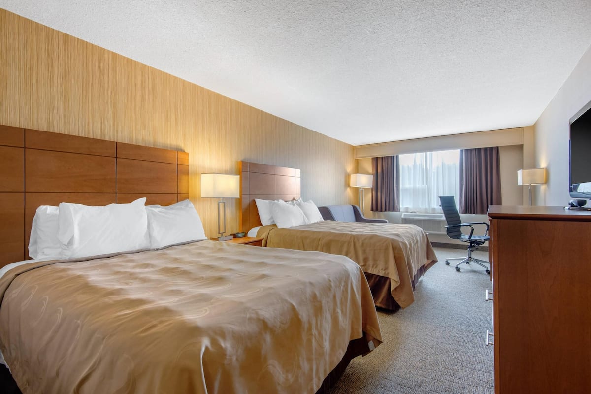 A hotel room with two beds, a desk, and a chair.
