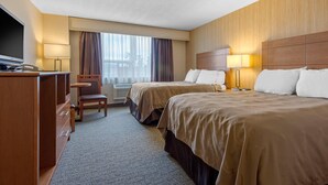 Habitación de hotel con dos camas, un escritorio con teléfono, una silla y un amplio ventanal con cortinas.