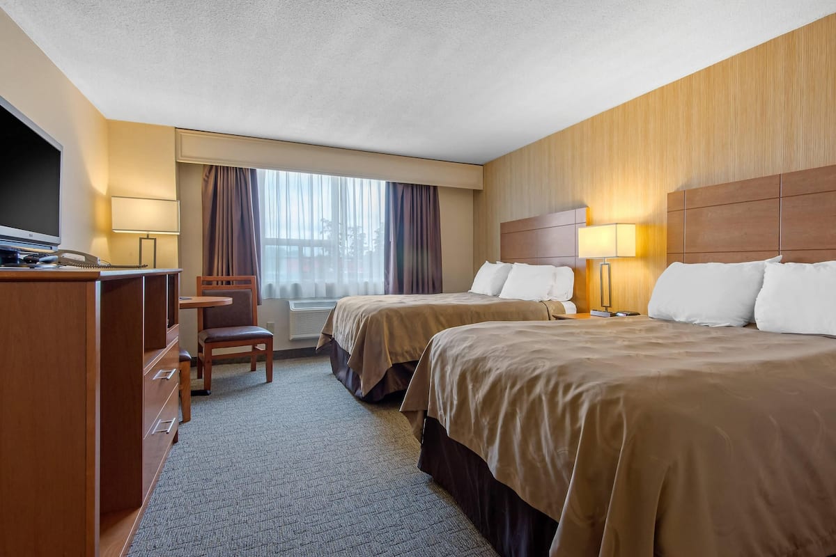 A hotel room with two beds, a desk with a telephone, a chair, and a large window with curtains.