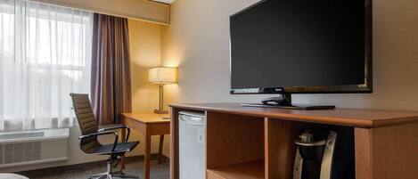 A hotel room with a bed, a desk with a chair, a television, a coffee maker, and a mini-fridge.