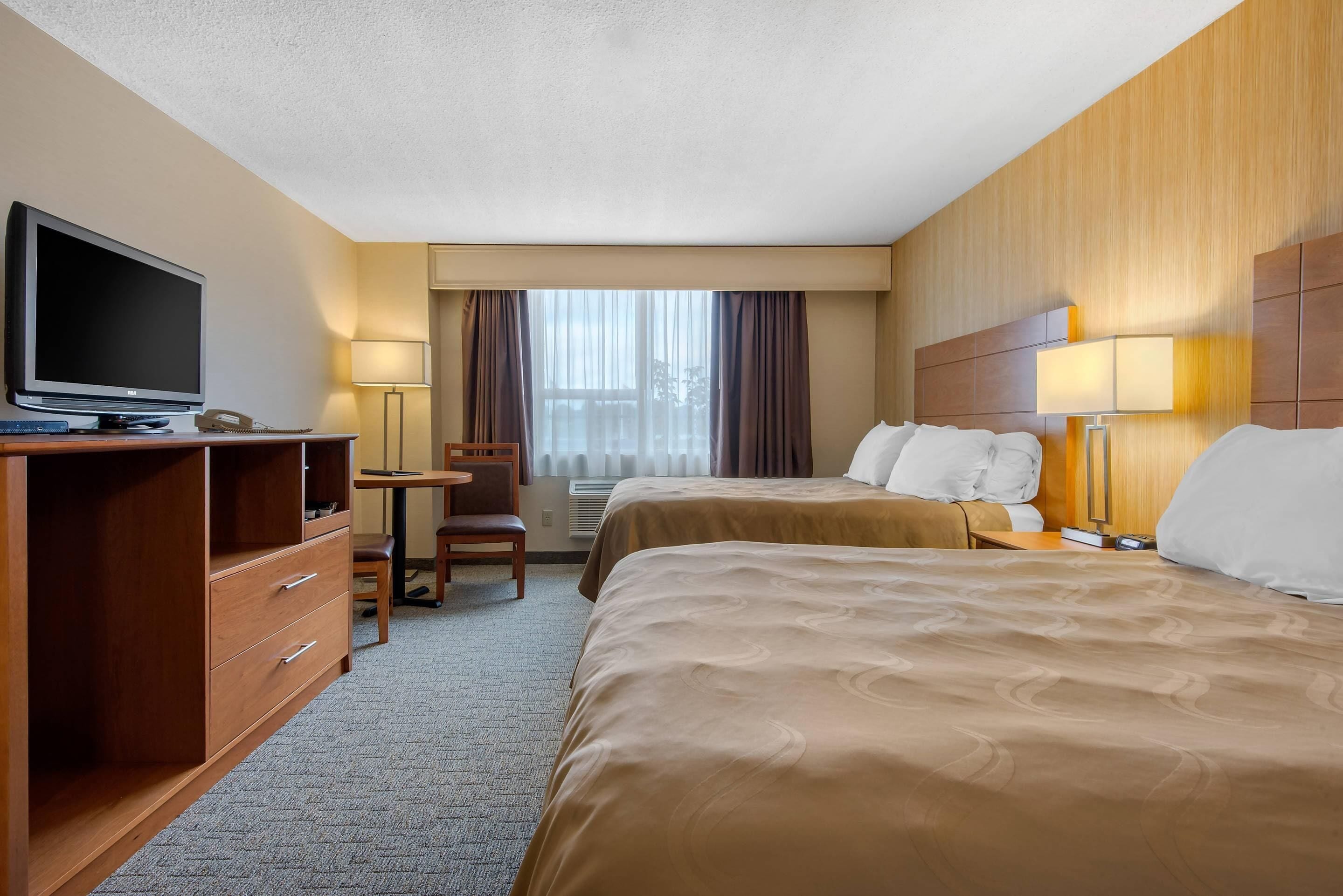 Une chambre d’hôtel avec deux lits, un bureau avec une chaise, une télévision et une lampe.