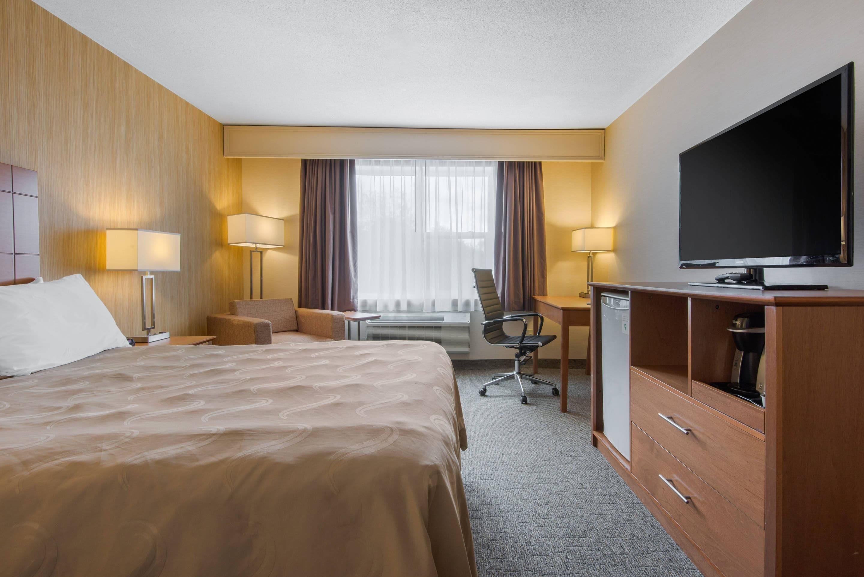A hotel room with a large bed, a desk with a chair, a television, and a cabinet.