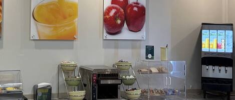 Una barra de desayuno con una máquina de café, cuencos de fruta y dispensador de jugo.