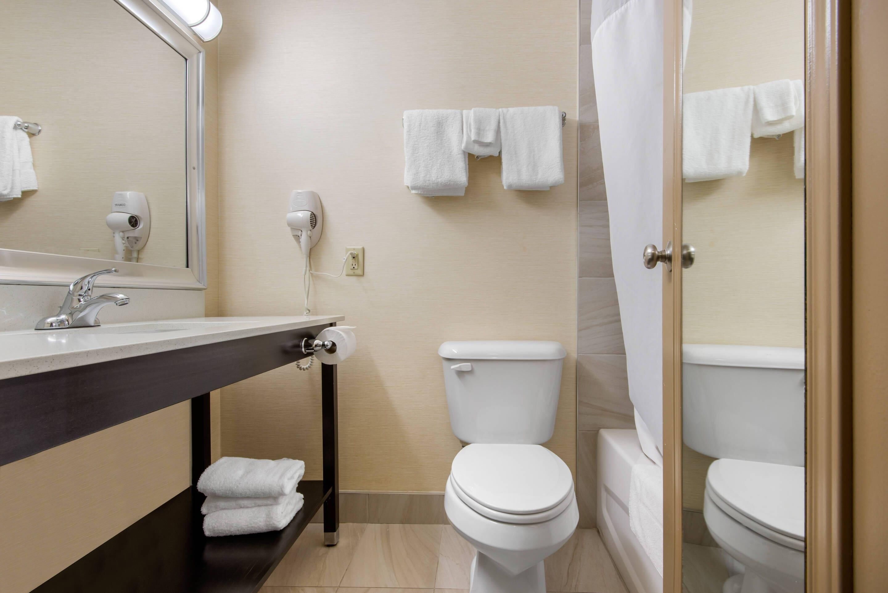Un baño con lavamanos, dos inodoros, un espejo y un perchero para toallas.