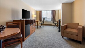 Habitación de hotel con televisión de pantalla plana, escritorio de madera, sillón marrón y dos sillas de oficina.