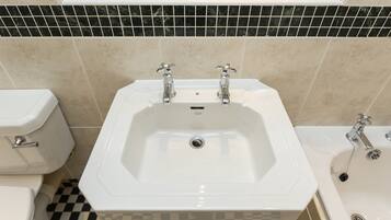 Un baño con lavamanos blanco, dos grifos, un inodoro y una bañera.