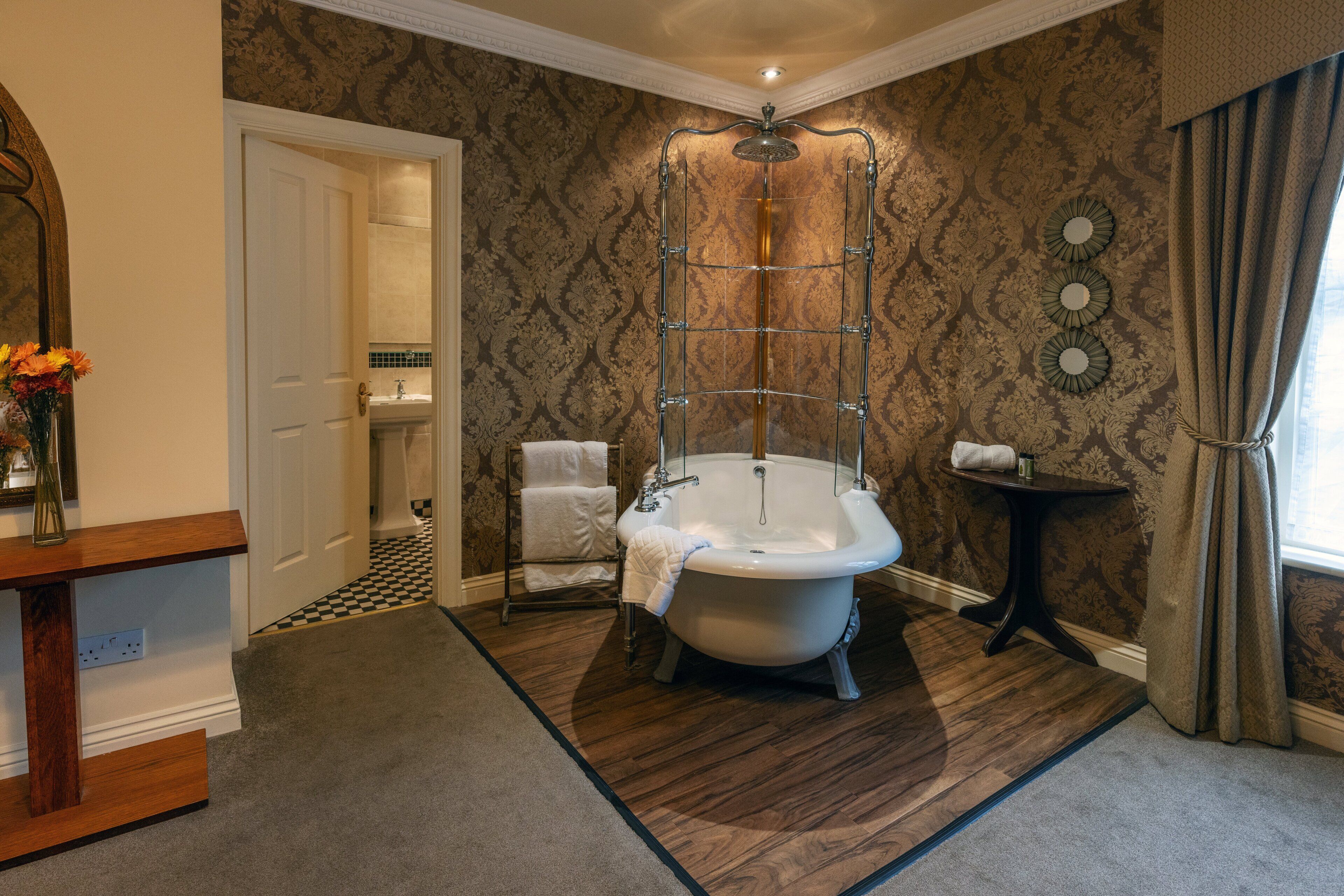 Een badkamer met een vrijstaand bad, een douchecabine, een wastafel met spiegel en een klein tafeltje met een handdoek.