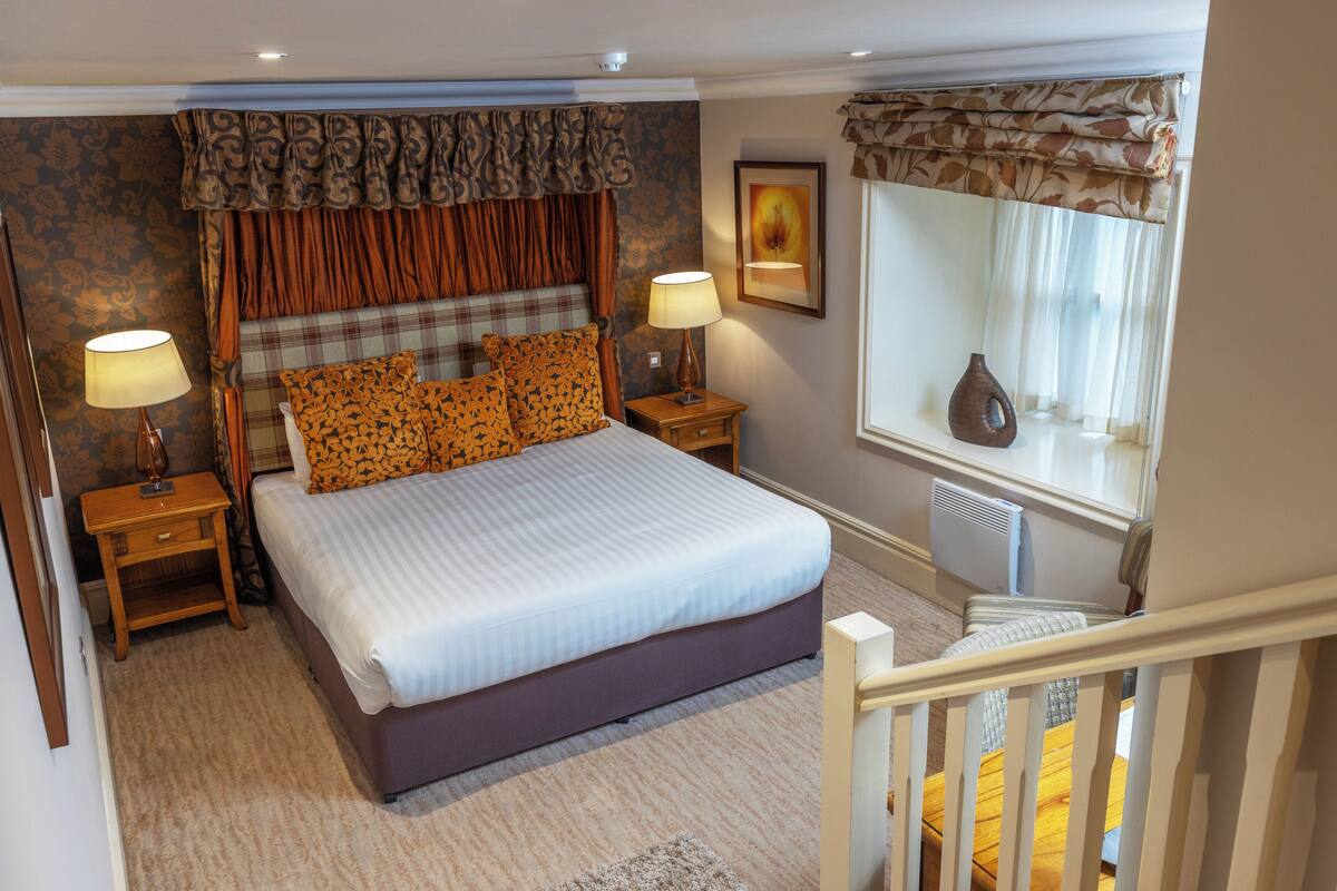 A bedroom with a large bed, two bedside tables, a nightstand, a window with curtains, and a radiator.