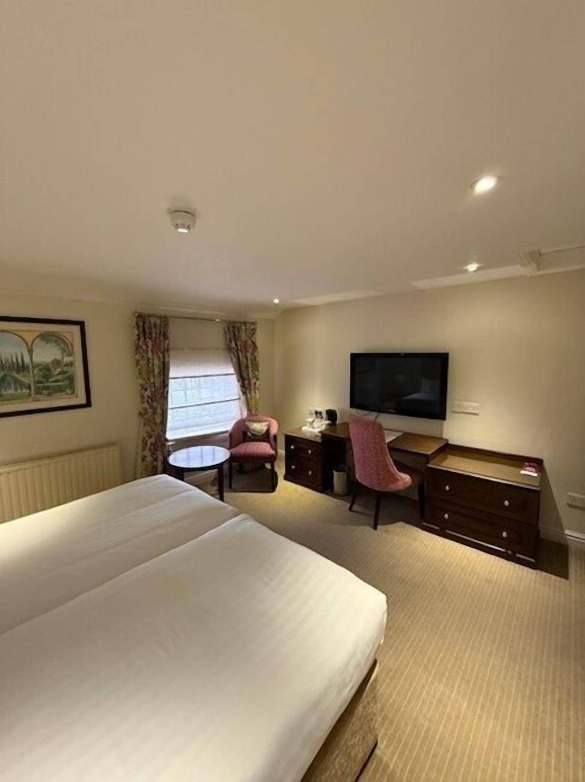 A hotel room with a large bed, a desk with a chair, a television, and a window with curtains.