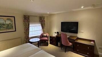 A hotel room with a large bed, a desk with a chair, a television, and a window with curtains.