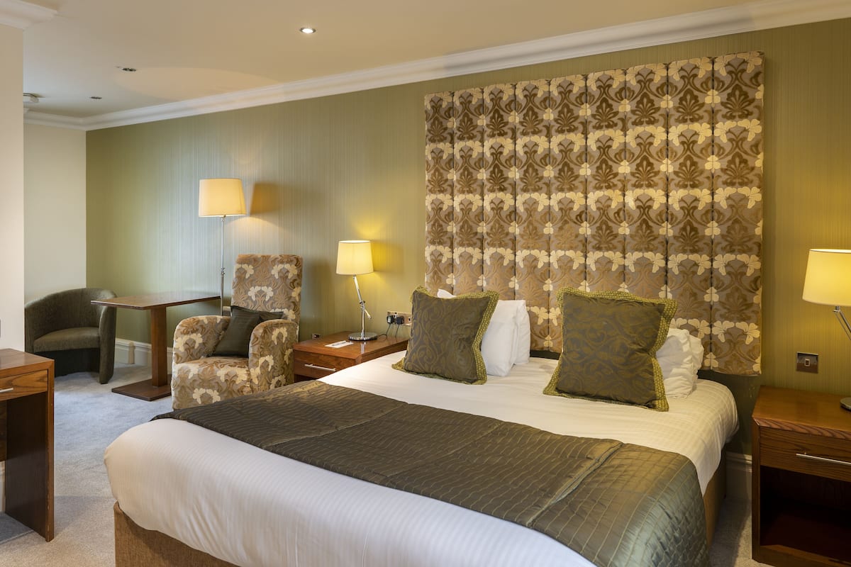 A hotel room with a large bed, two bedside tables, a chair, and a desk.