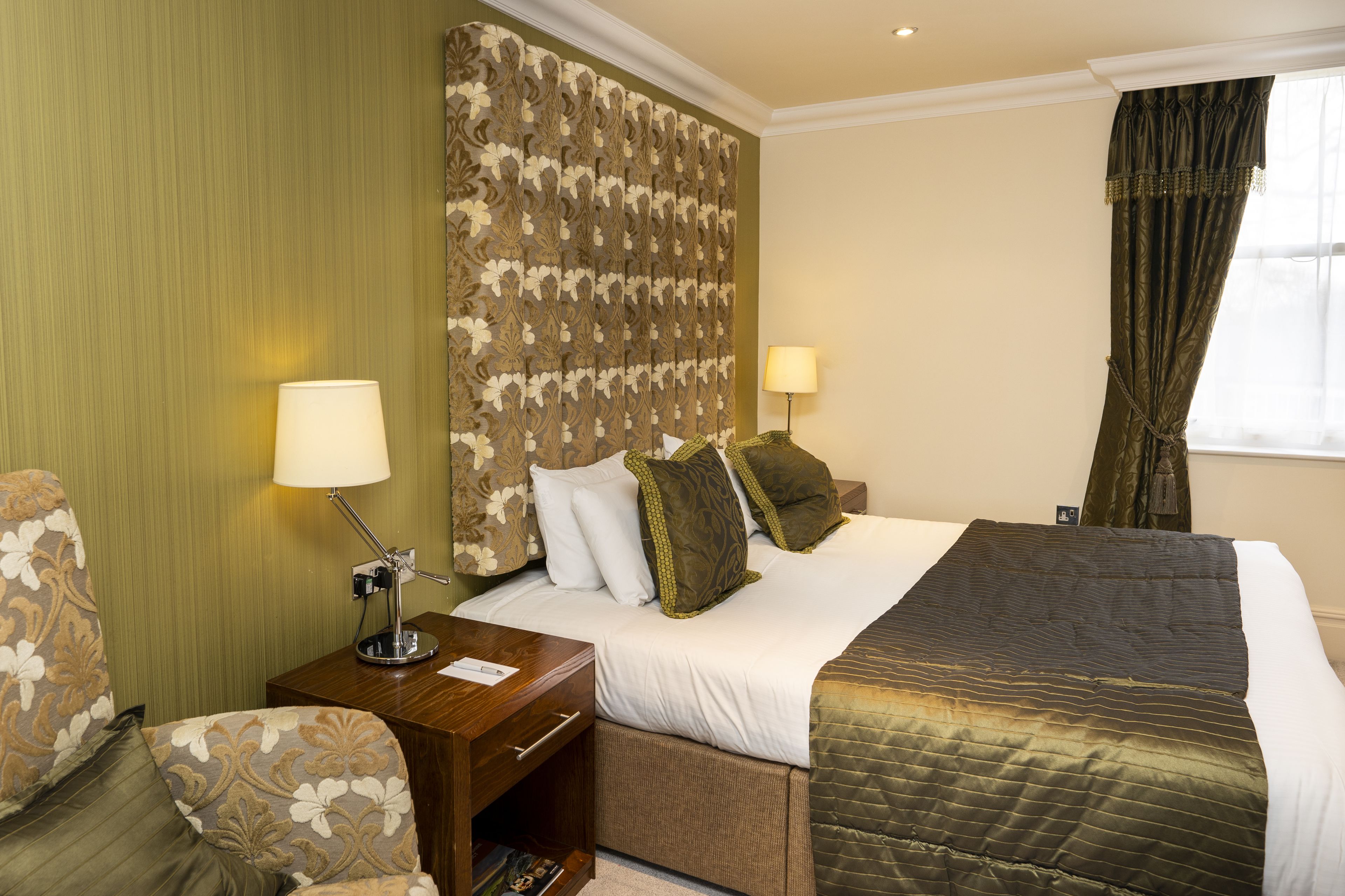 Habitación de hotel con cama, dos lámparas de noche, mesita de noche, una silla y una ventana con cortinas.