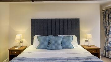 Una cama bien tendida con un cabecero estampado, dos lámparas de noche y una cortina con motivos florales.