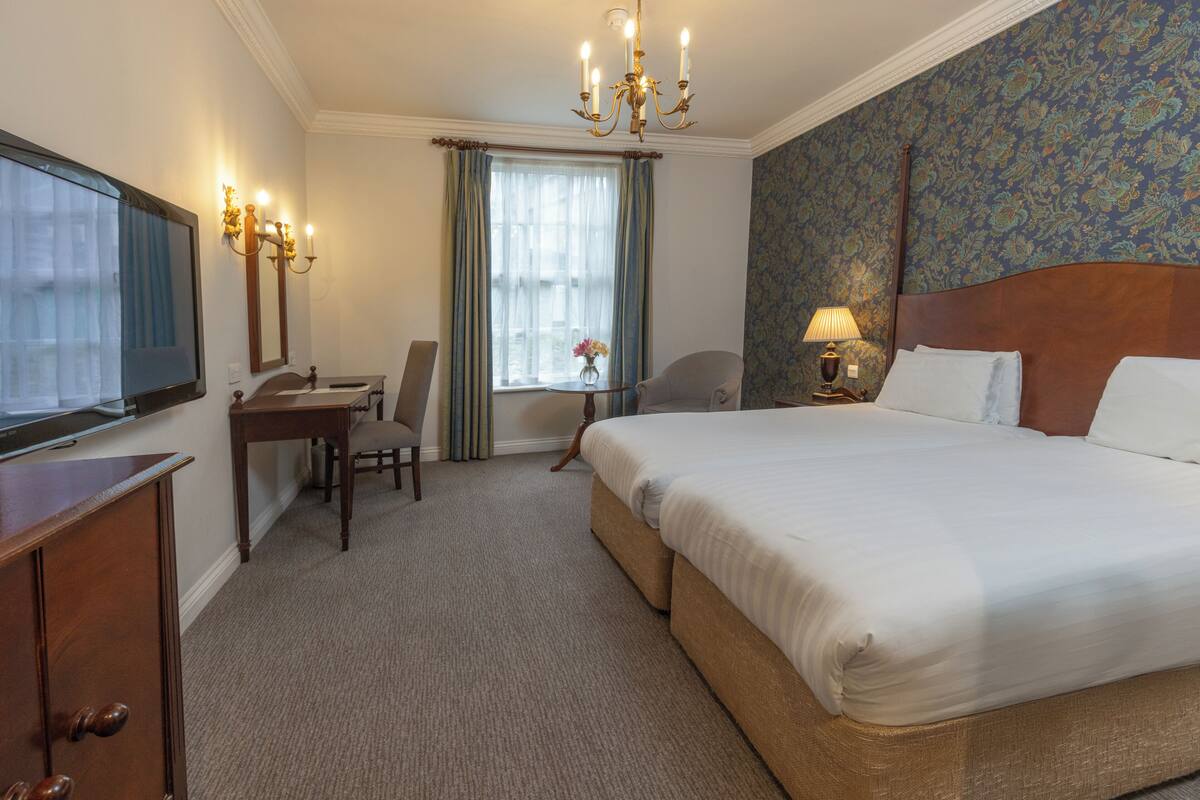 A hotel room with a bed, a desk, a chair, a television, a lamp, and a window with curtains.