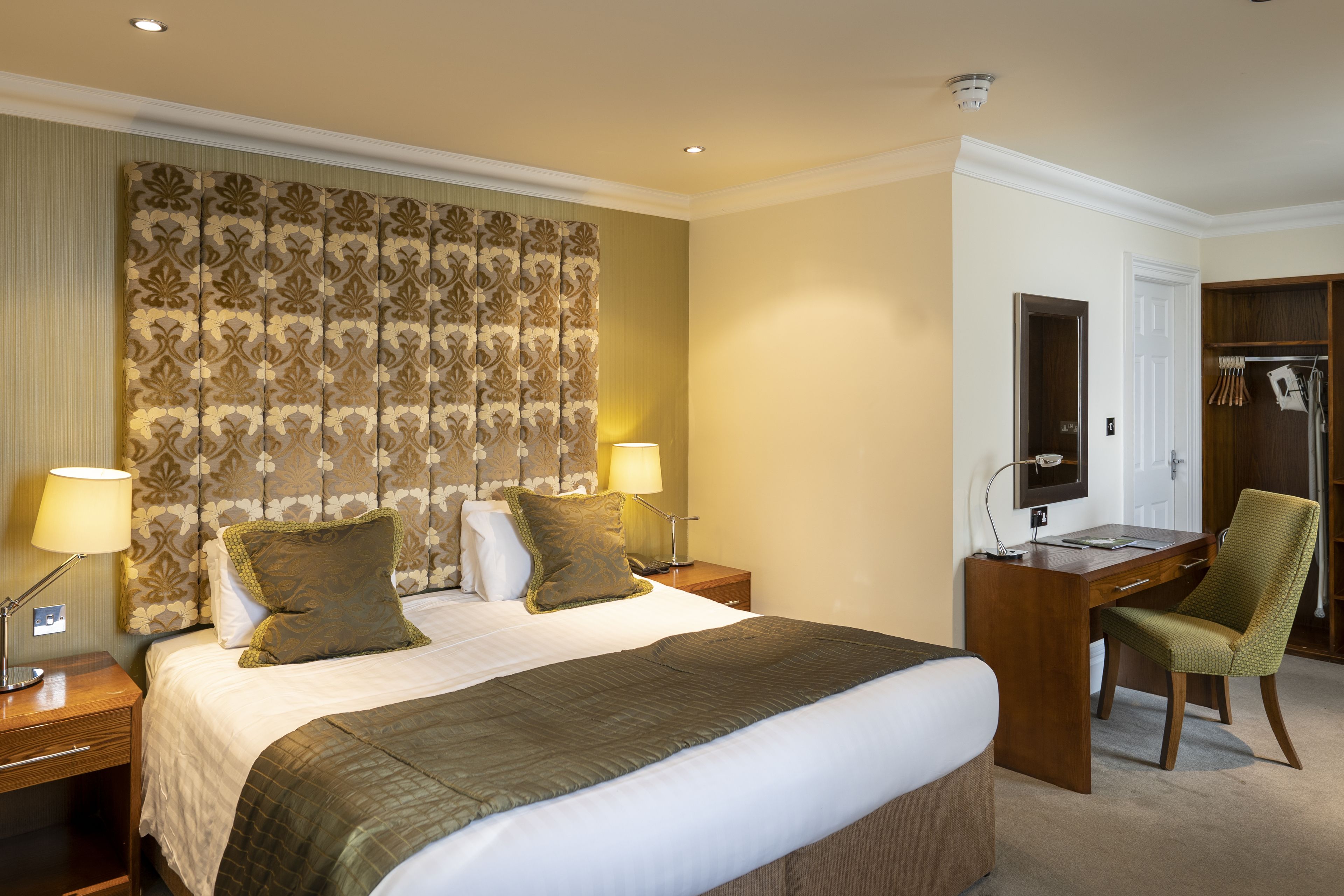 A hotel room with a large bed, two bedside lamps, a desk with a chair, and a wardrobe.