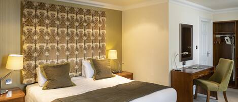 A hotel room with a large bed, two bedside lamps, a desk with a chair, and a wardrobe.
