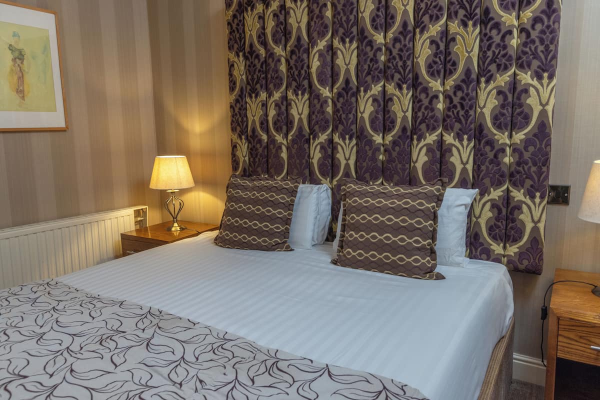 A neatly made bed with patterned bedding, a headboard with a floral design, and bedside lamps.