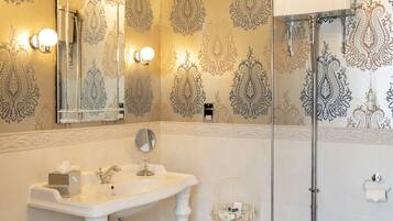 A bathroom with a white sink, mirror, and toilet, featuring ornate wallpaper and a chandelier.