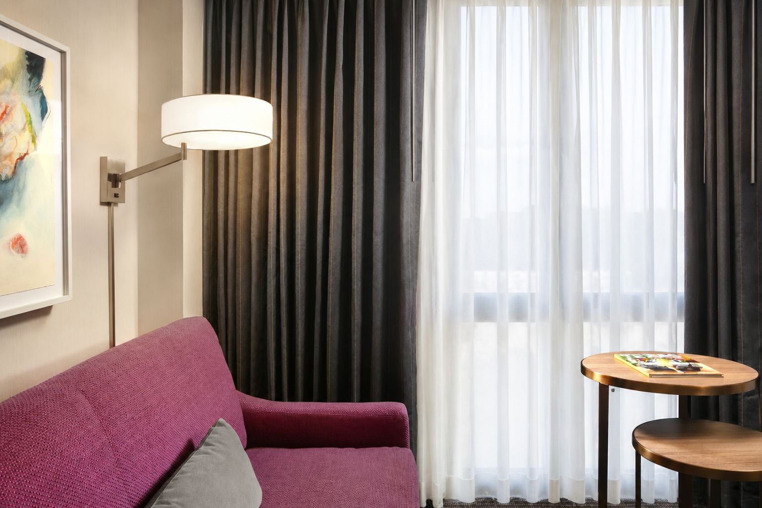 Una habitación con un sofá morado, una mesita redonda con revistas, una lámpara de pie y un cuadro en la pared.