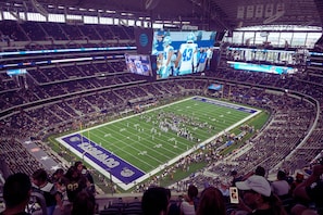 A large stadium with multiple levels of seating, a football field, and a large screen displaying an event.