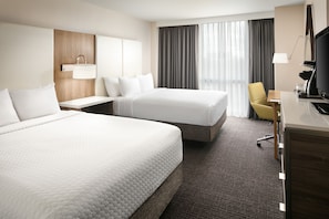 A hotel room with two beds, a desk, a chair, a TV, and a window with curtains.