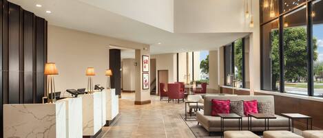 A modern lobby with a reception desk, seating area, and large windows offering views.