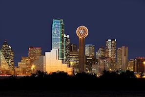 A city skyline at night with illuminated buildings and a distinctive spherical structure.