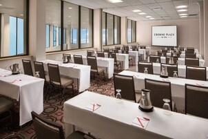 A conference room with multiple tables, chairs, and a projection screen displaying "CROWNE PLAZA BY IHG".