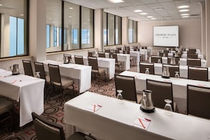 A conference room with multiple tables, chairs, and a projection screen displaying "CROWNE PLAZA BY IHG".
