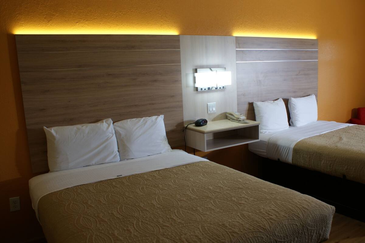A hotel room with two beds, a bedside table with a lamp, a phone, and a red chair.