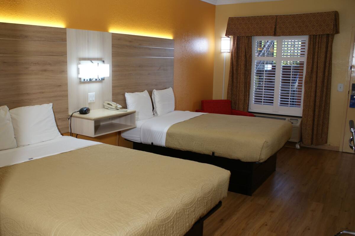 A hotel room with two beds, a desk, a phone, and a window with blinds.