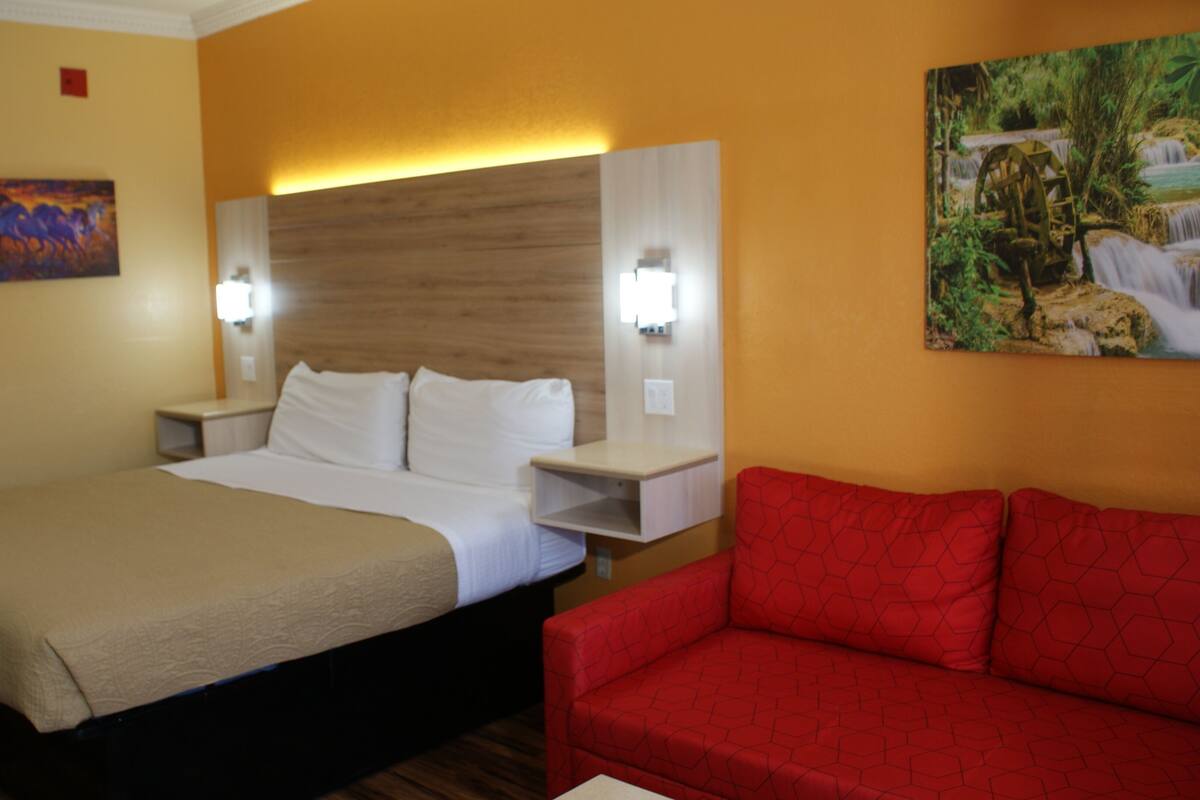 A hotel room with a large bed, a red sofa, and a painting on the wall.