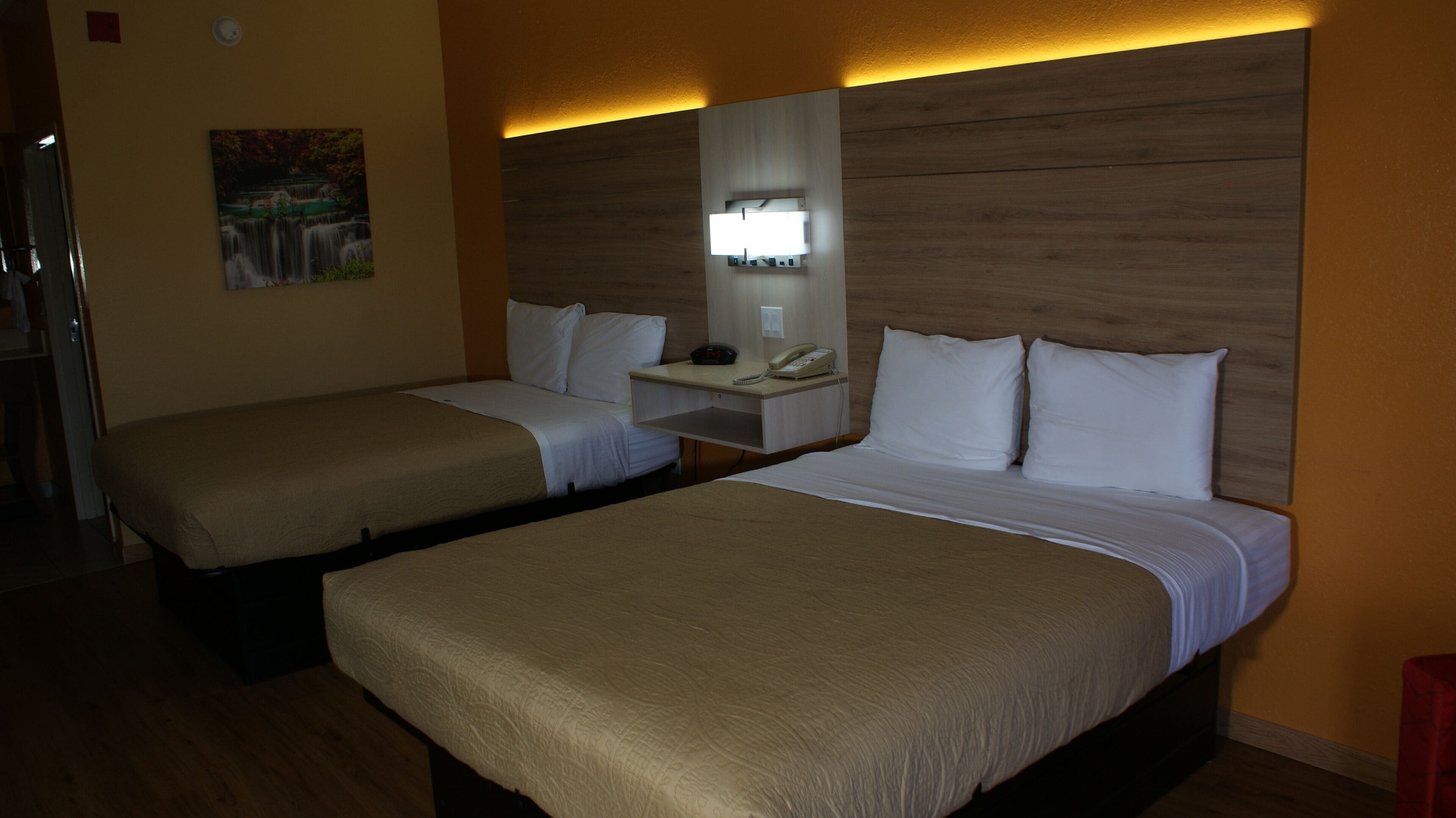 Ein Hotelzimmer mit zwei Betten, einem Nachttisch mit Lampe, einem Gemälde an der Wand und einem hölzernen Kopfteil.