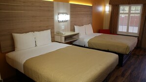 Habitación de hotel con dos camas, una mesita de noche con teléfono, lámpara y ventana con persianas.