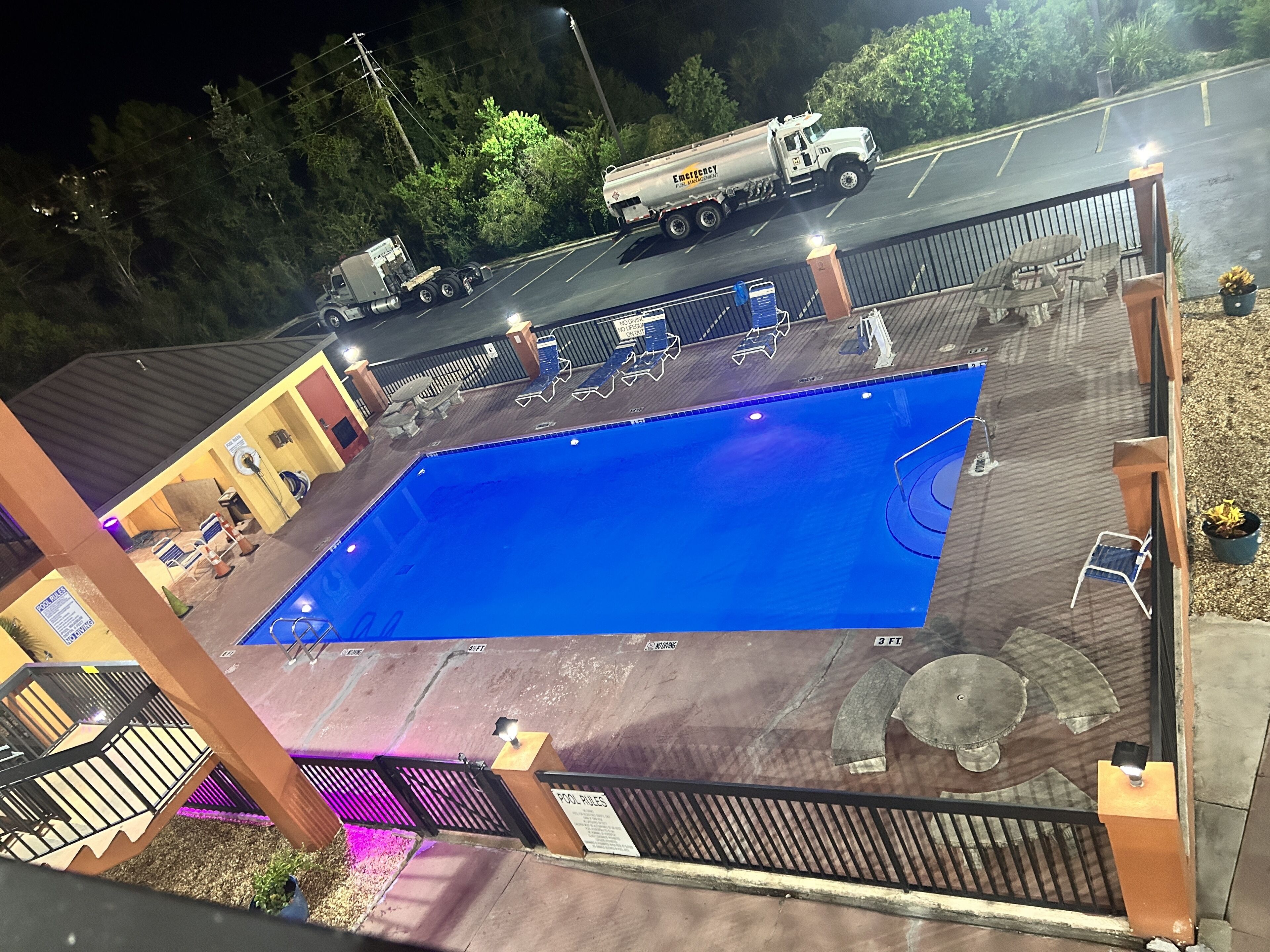 A swimming pool with a deck area, a covered seating area, and a truck parked nearby.