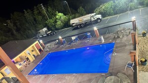 Una piscina con zona de solárium, un área de estar cubierta y una camioneta estacionada cerca.