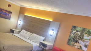 Una habitación de hotel con cama, sofá rojo, una mesita y un cuadro en la pared.