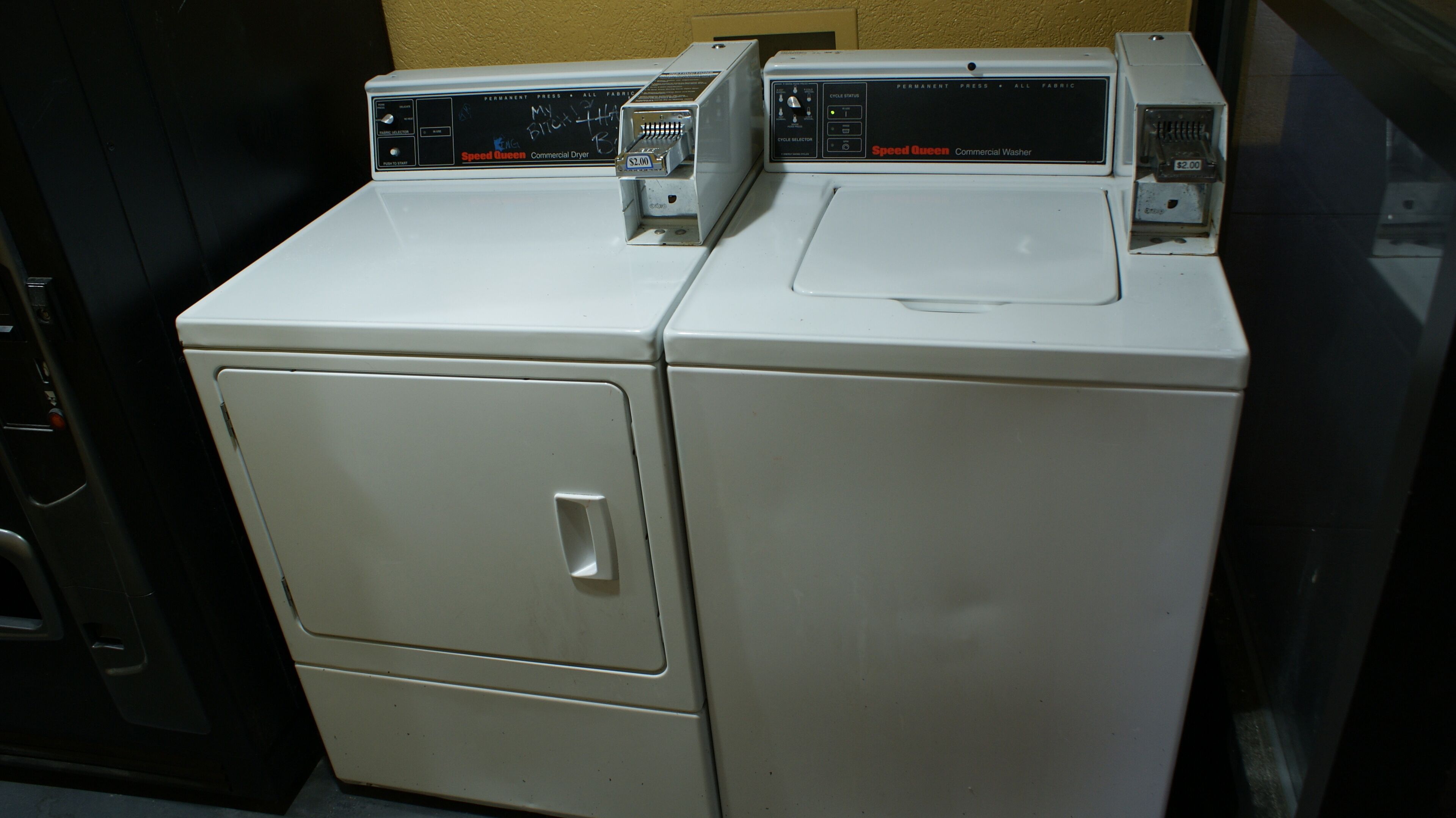 Two white commercial washers with control panels, a door, and a price tag of $2.00.