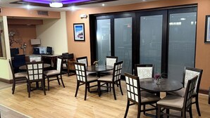 Un comedor con suelo de madera, sillas oscuras con asientos acolchados y una mesa central.