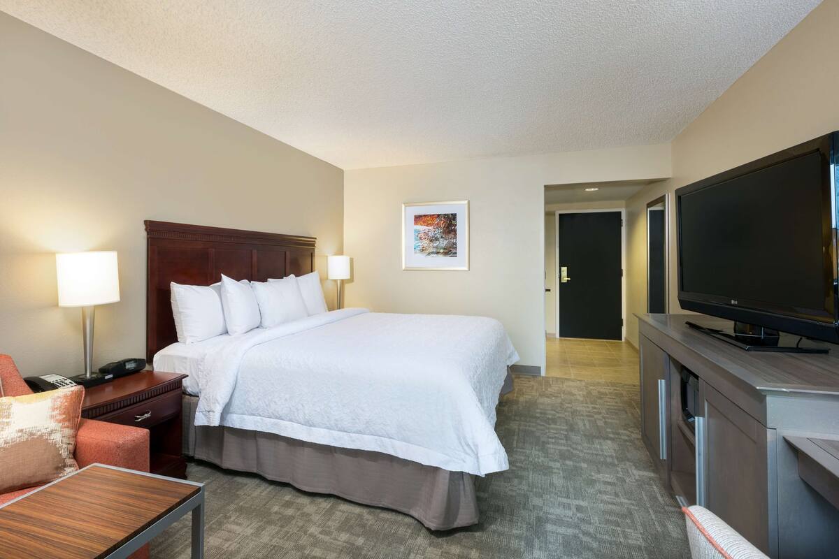 A hotel room with a large bed, bedside lamps, a flat-screen TV, a desk, and a chair.