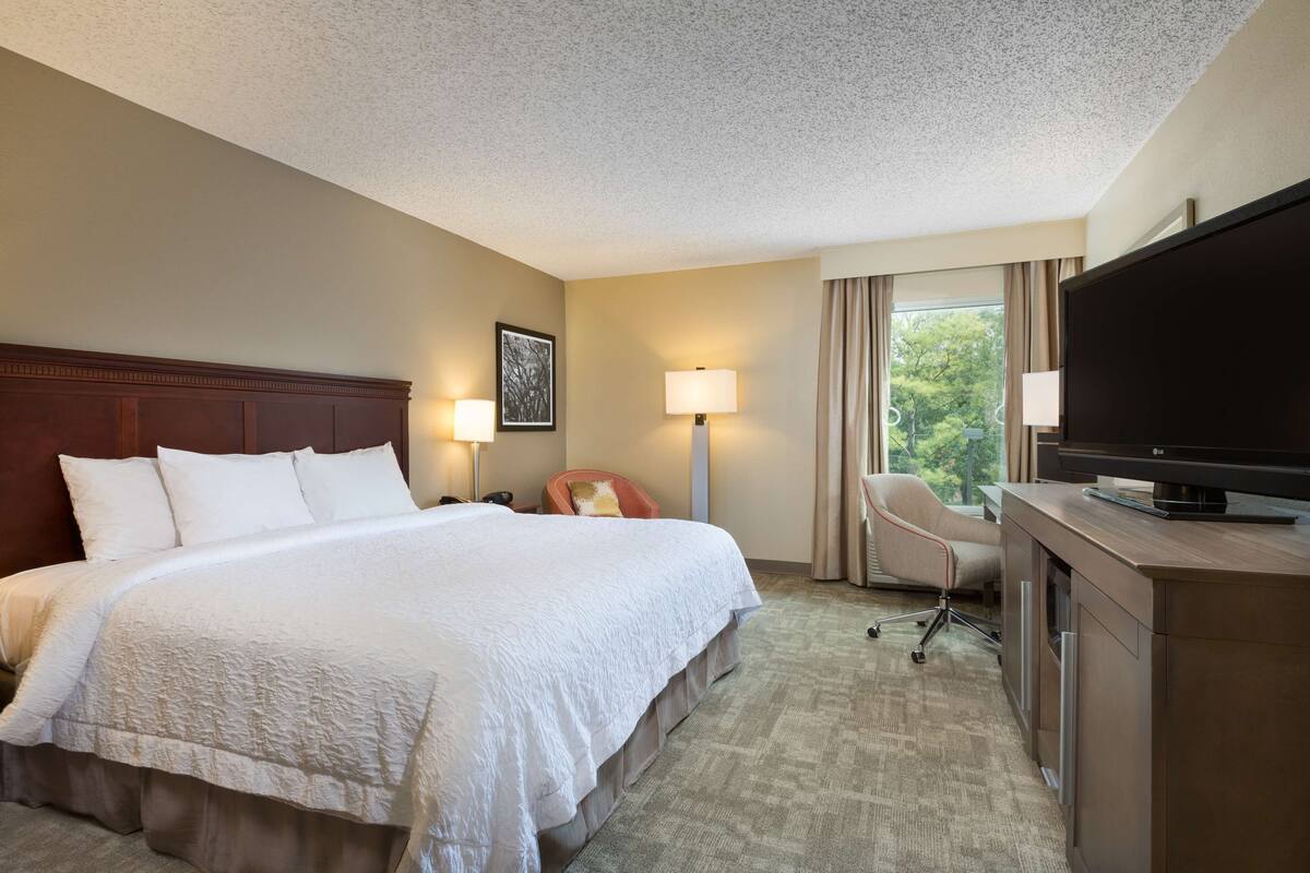 A hotel room with a large bed, a desk with a TV, two lamps, and a chair.