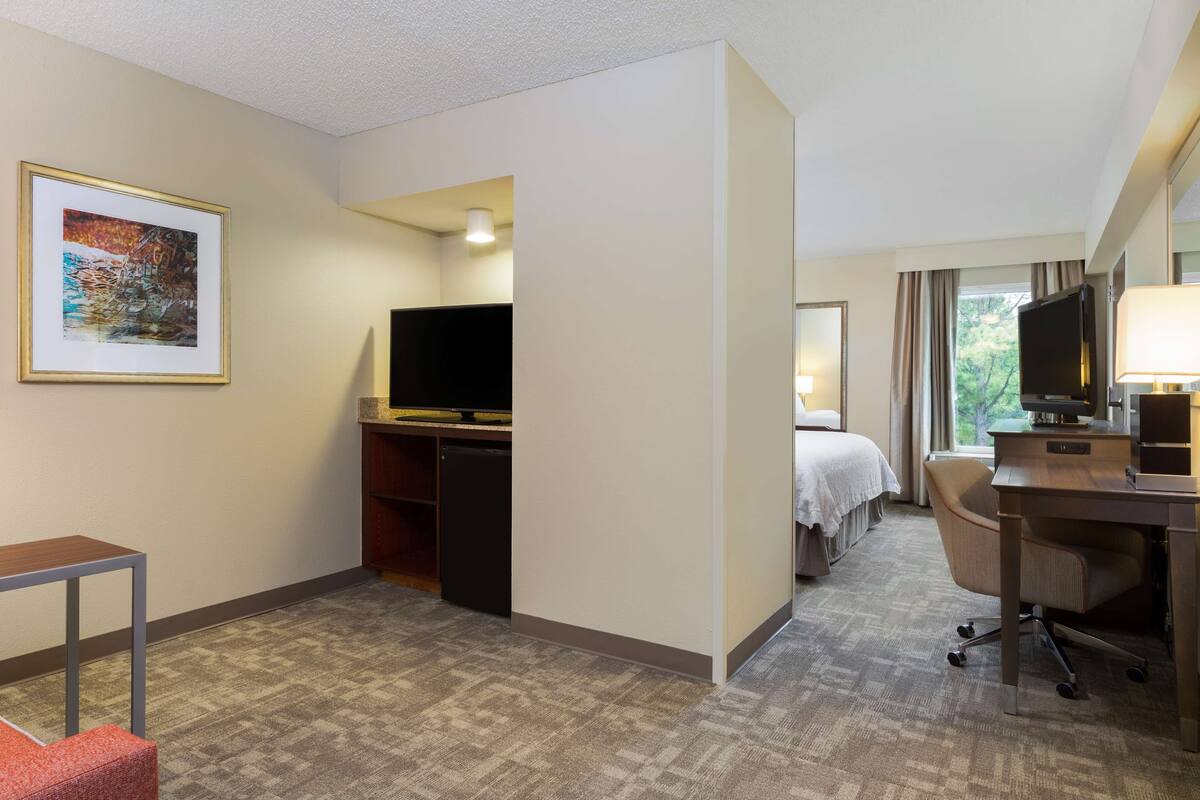 A hotel room with a bed, a desk, a chair, a television, and a framed picture on the wall.