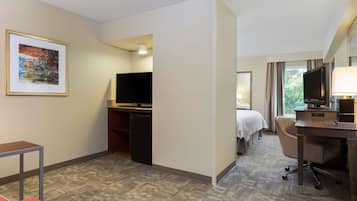 A hotel room with a bed, a desk, a chair, a television, and a framed picture on the wall.