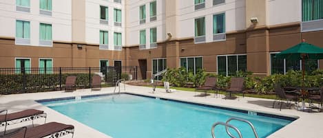 A hotel pool area with a clear blue pool, lounge chairs, and a covered seating area.