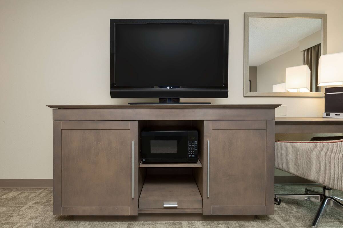 A flat-screen TV mounted above a wooden cabinet with a microwave inside.