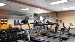 Un gimnasio con cintas de correr, mancuernas y bicicletas estáticas.
