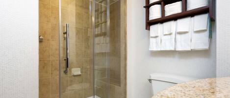 Une salle de bain avec une douche à parois de verre, des toilettes et une étagère avec des serviettes.