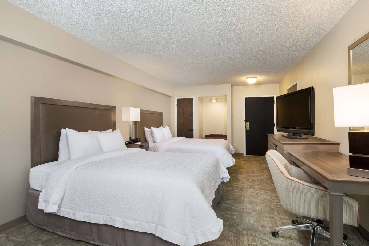 A hotel room with two beds, a desk with a computer, and a TV.