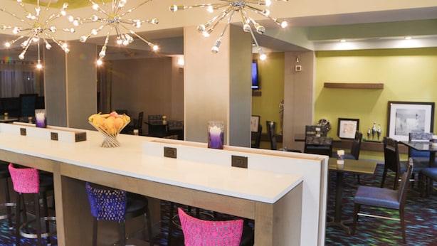 Um saguão de hotel com um balcão de recepção comprido, banquetas de bar coloridas e um lustre.