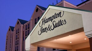 Placa de hotel com a inscrição 'Hampton Inn & Suites', apresentando um estilo arquitetônico clássico.